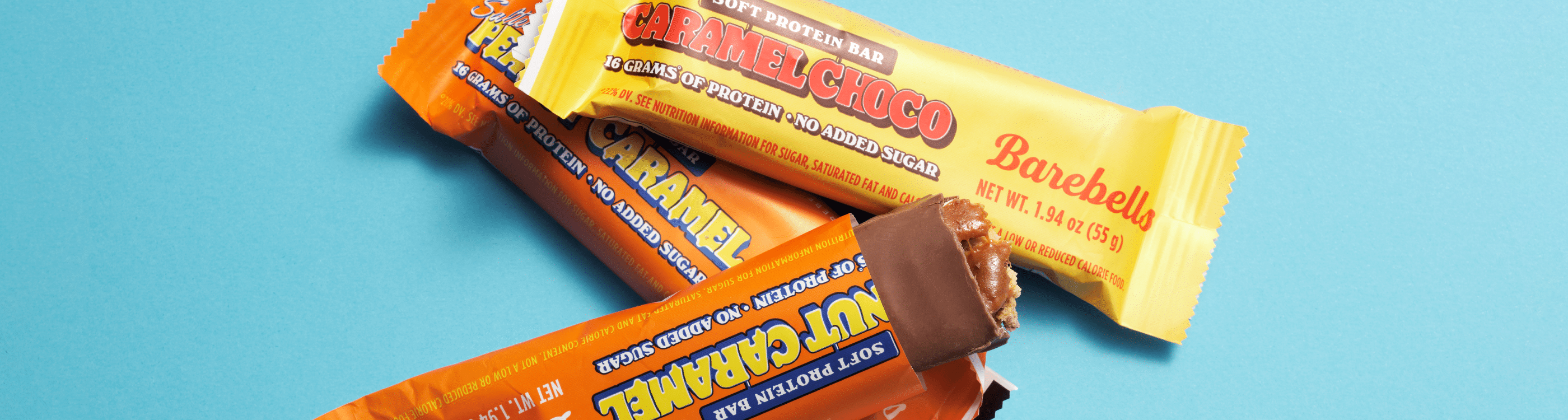 Verschiedene Proteinriegel auf blauem Hintergrund, einer geöffnet mit sichtbarem Karamell.